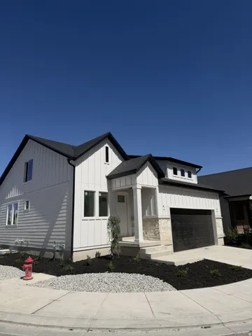 Crisp white siding, black-trimmed windows, a dark shingle roof, a two-car garage, and stone facade accents