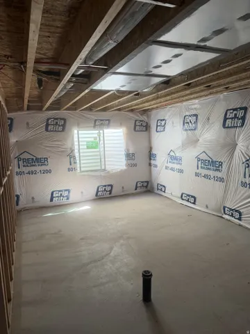 Unfinished basement area featuring exposed wood joists and subfloor above, concrete flooring, and an egress window