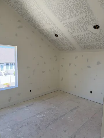 Vaulted ceiling with textured finish, recessed lighting provisions, window with white trim, and unfinished flooring