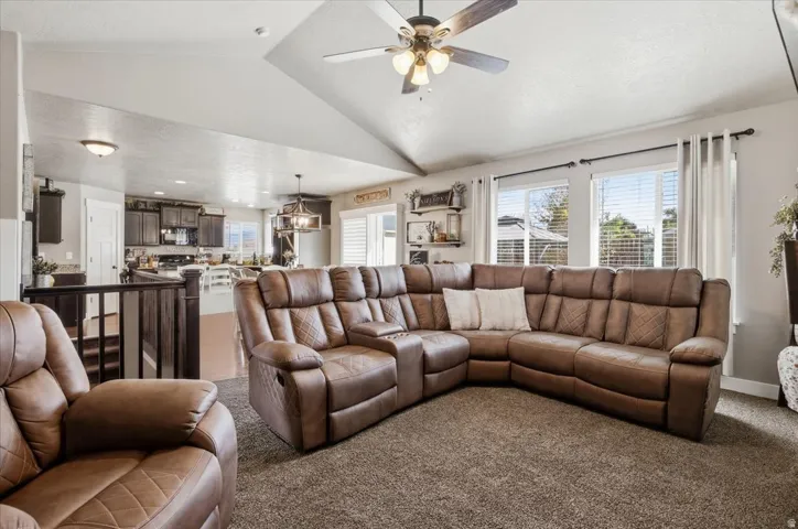 Open-concept living area with vaulted ceilings, a ceiling fan, carpet flooring, and abundant natural light from multiple windows