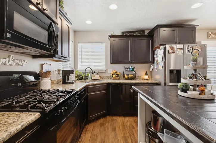Kitchen featuring dark wood cabinetry, light-toned granite countertops, and stainless steel appliances including a built-in microwave and refrigerator