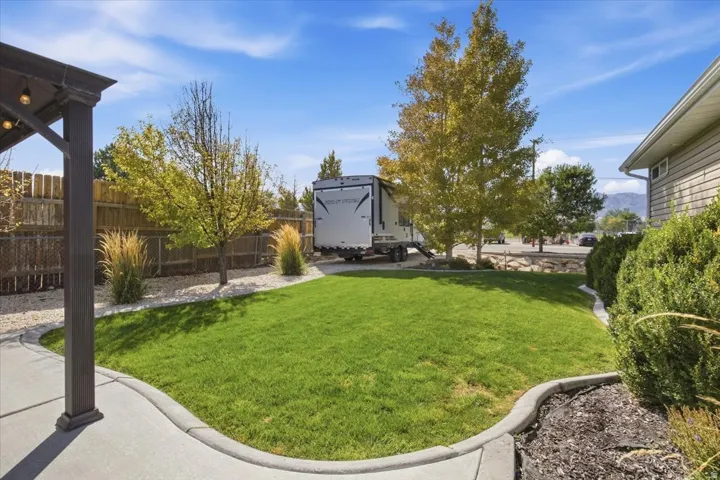 Manicured lawn, concrete patio, garden beds with landscaping, wood fence, and mature trees