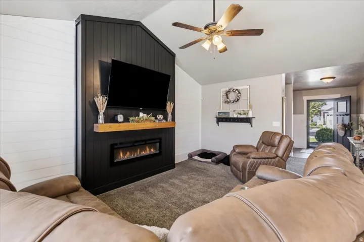 Living area featuring a textured accent wall with an integrated electric fireplace, wood mantel, and vaulted ceilings