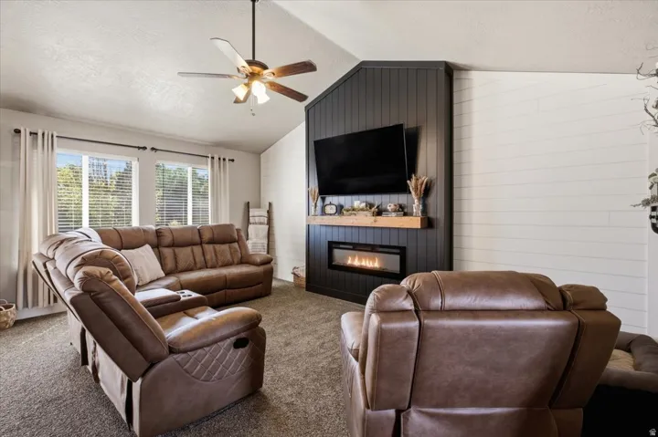 Vaulted ceiling with a ceiling fan, dual windows, and an electric fireplace with a wood mantel