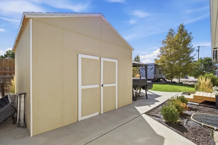 Detached storage shed with double doors, concrete walkway, and landscaped garden beds