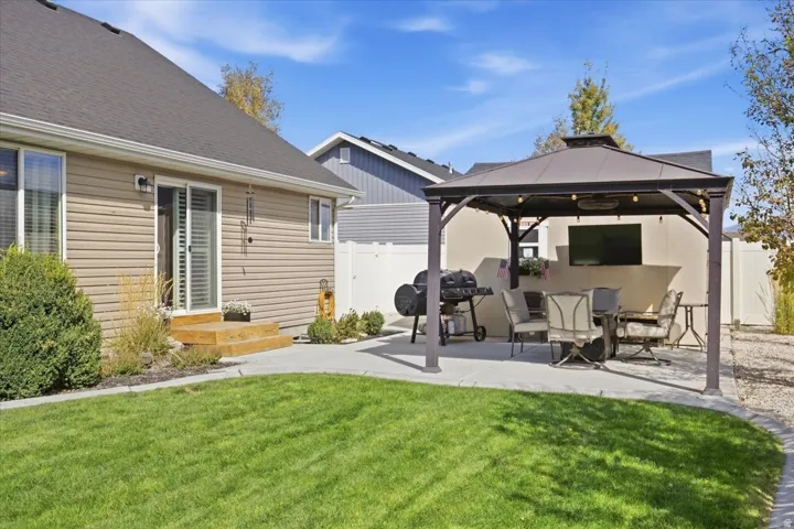 Manicured lawn, concrete patio, wood steps, sliding glass door, and a built-in gazebo