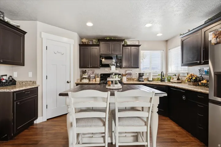 Dark wood-finish cabinetry, granite countertops, wood-finish flooring, recessed lighting, and a kitchen island with seating