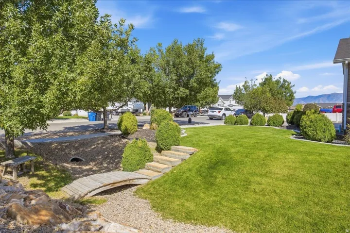 Lush green lawn with mature trees, decorative landscaping, and a wooden footbridge over a dry creek bed