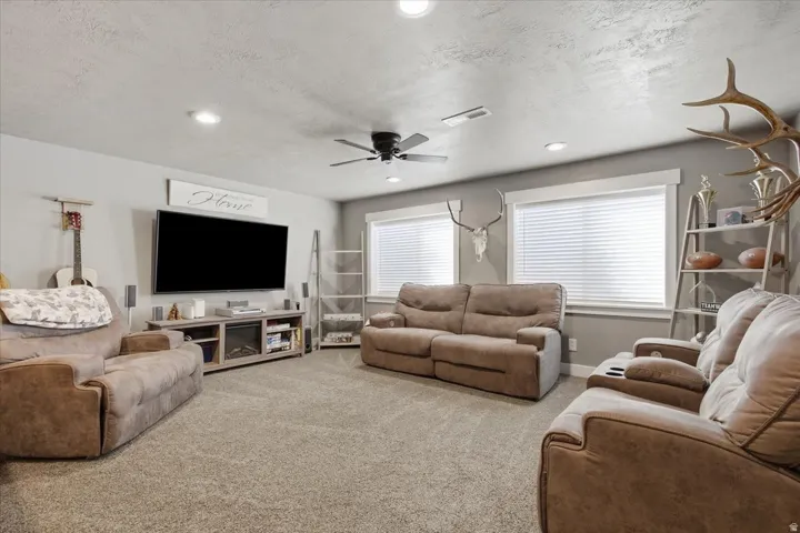 Recessed lighting, ceiling fan, two windows with white blinds, and a built-in media console with an electric fireplace
