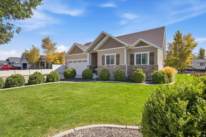 Expansive front lawn with layered landscaping, stone and siding exterior, multiple gables, and an attached two-car garage