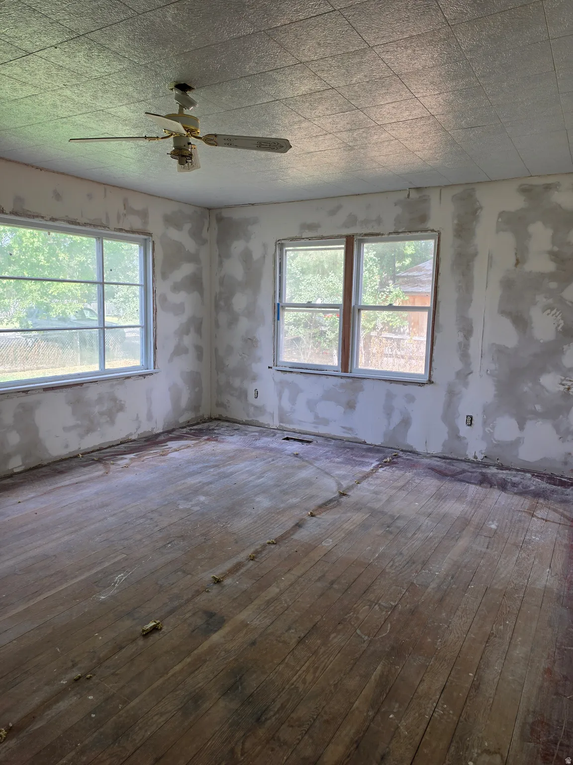 Wood-finish flooring, multiple windows, ceiling fan, and textured ceiling panels