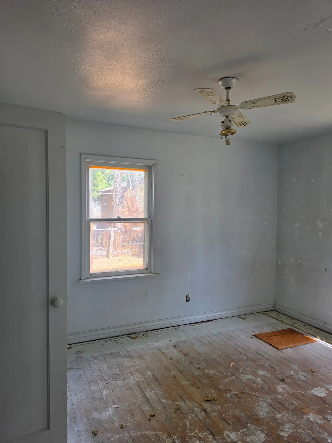 Wood-finish flooring with perimeter trim, a single window, and a ceiling fan