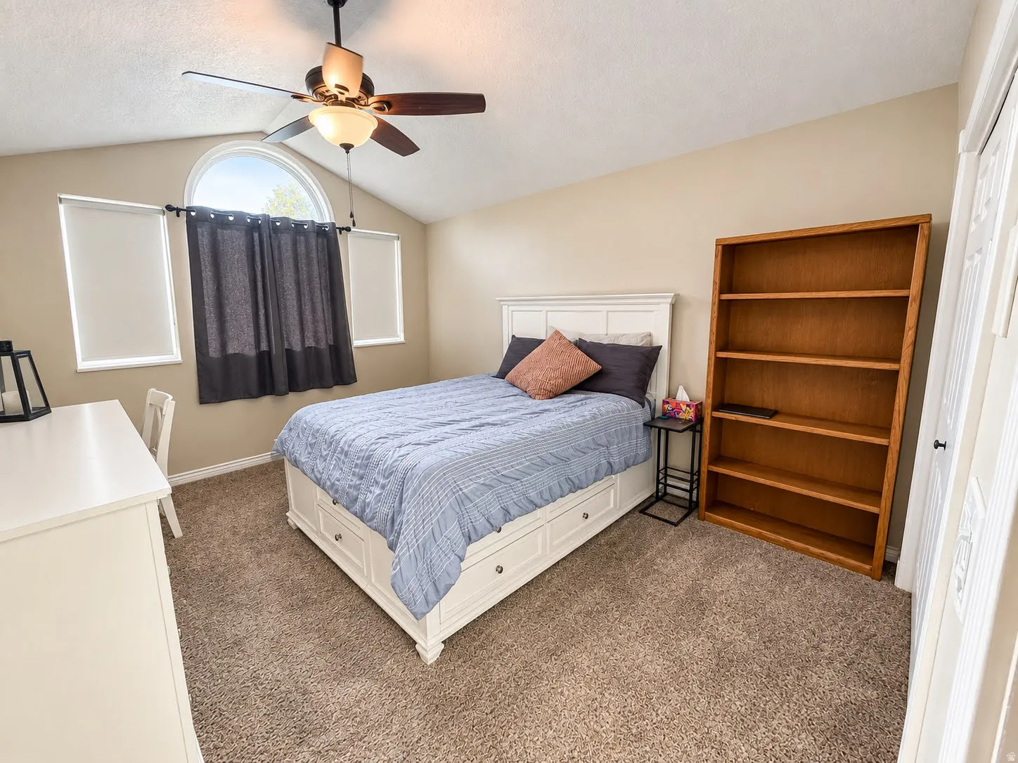 Arched window feature, vaulted ceiling, ceiling fan with light fixture, and plush carpeting