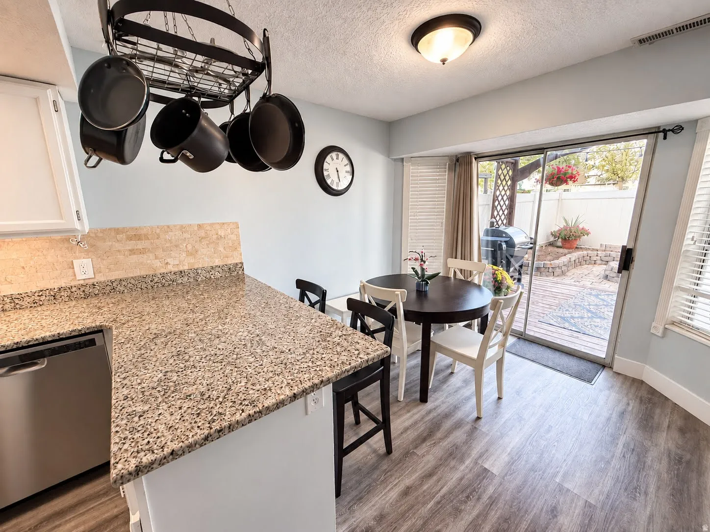 Kitchen dining area featuring granite-finish countertops, stainless steel appliance, wood-finish flooring, and direct access to an outdoor patio with privacy fencing