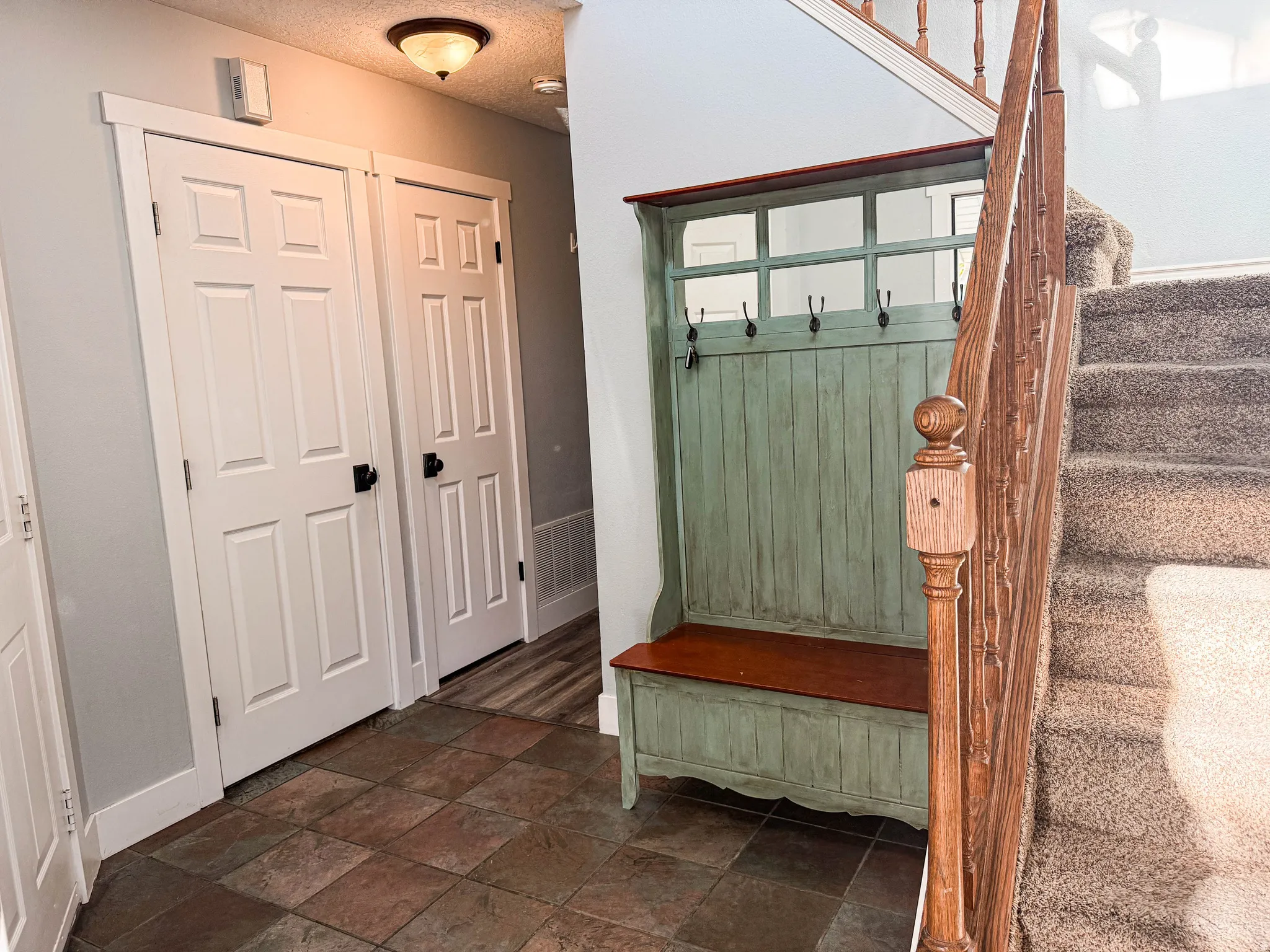 Tiled entry flooring, paneled interior doors with dark hardware, built-in coat rack, and carpeted staircase with wood banister