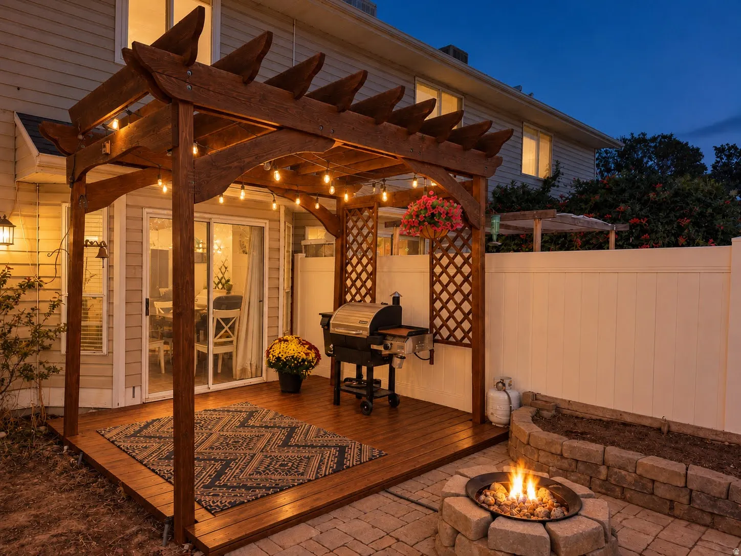 Wood pergola with string lighting, wood deck, sliding glass door, privacy fencing, and a stone fire pit