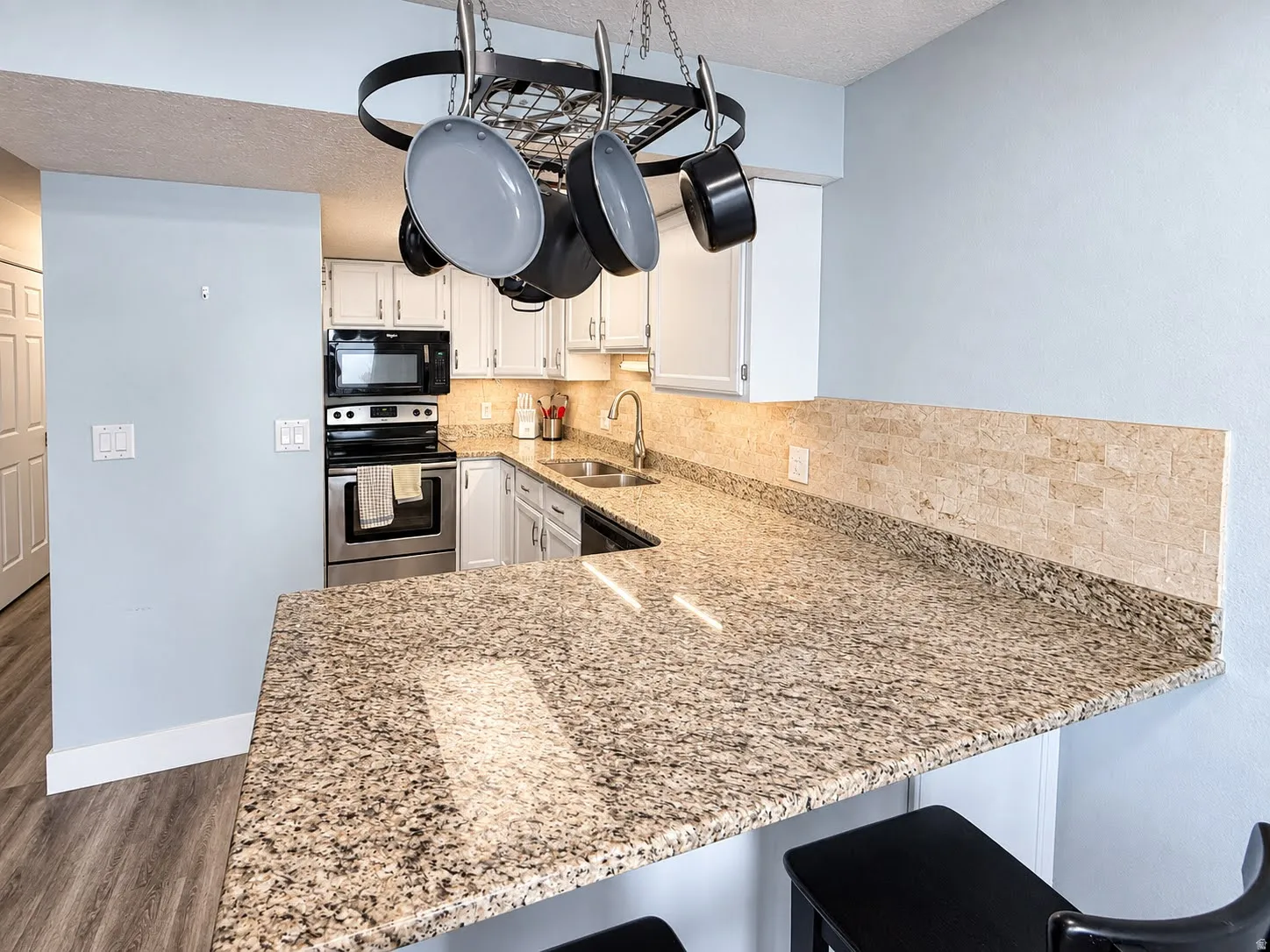 Kitchen featuring granite countertops, stainless steel appliances, white cabinetry, a tile backsplash, and wood-finish flooring