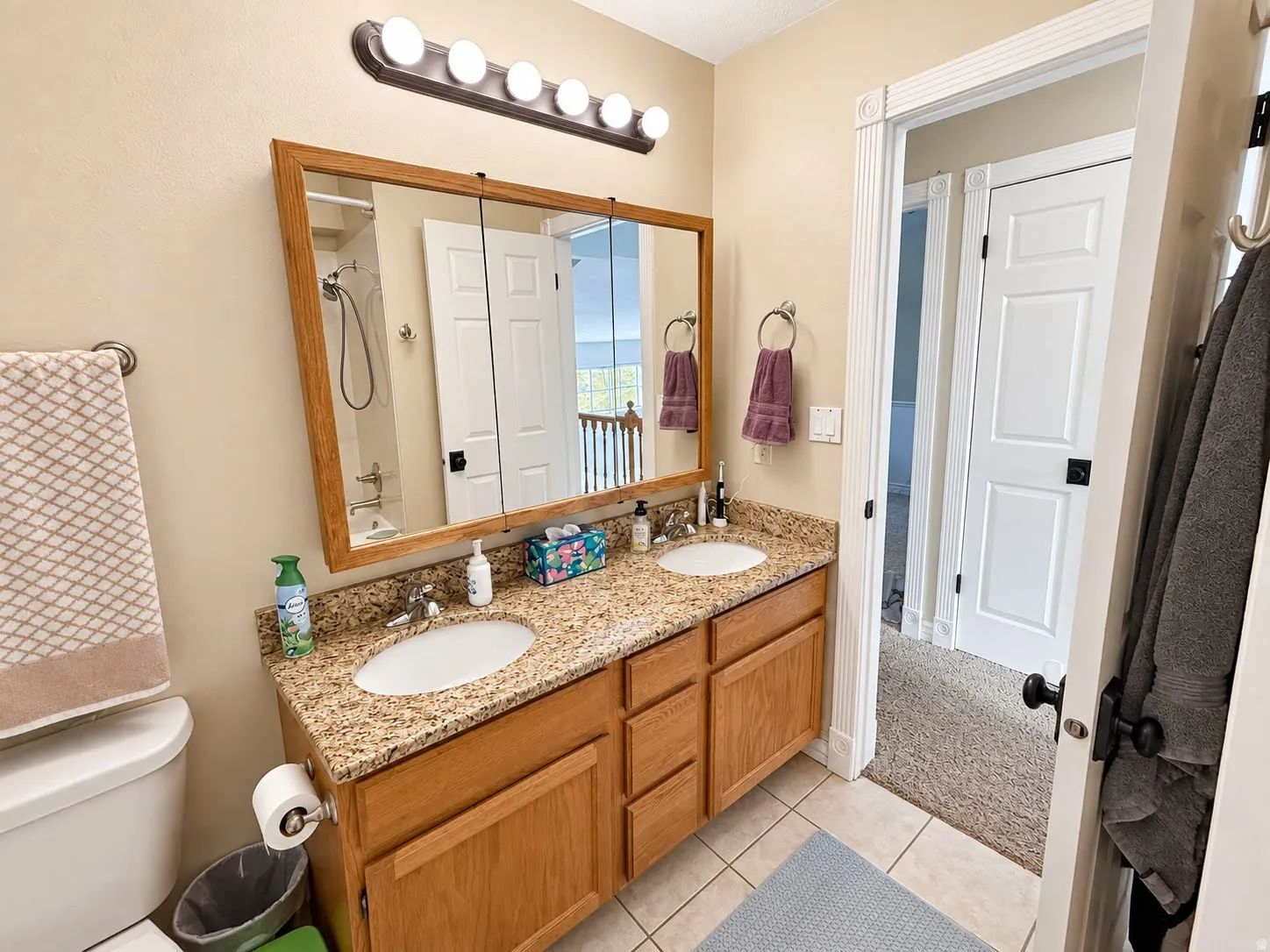 Dual white oval sinks, light wood-finish cabinetry, granite-finish countertop, and tile flooring