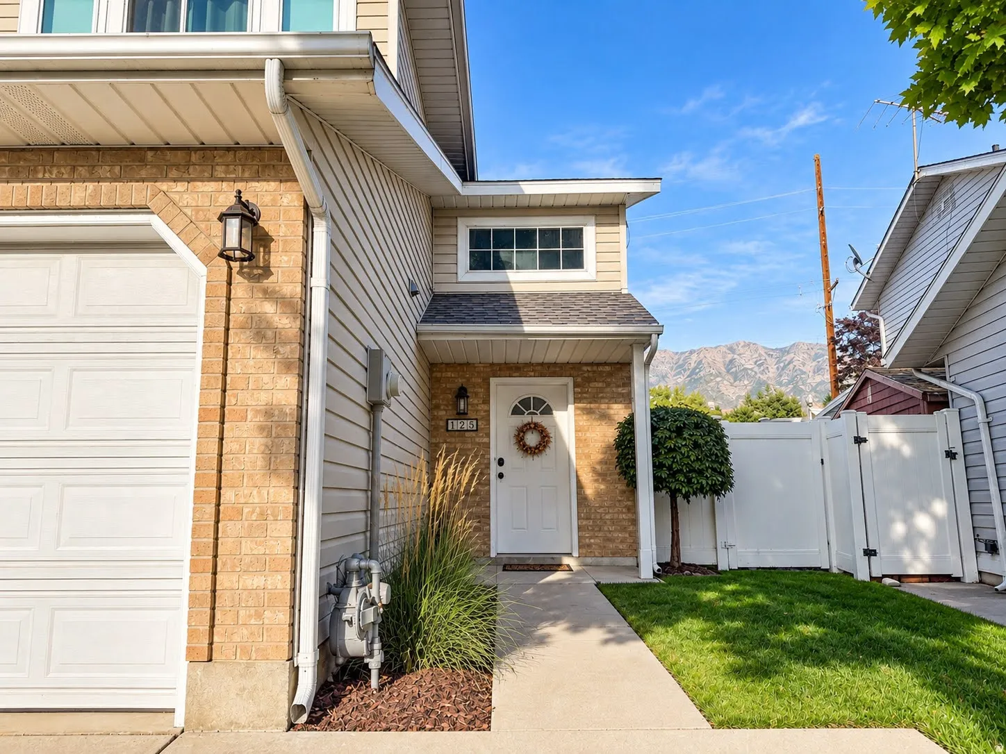 Brick and siding exterior with an attached garage, landscaped entry, and a mountain backdrop