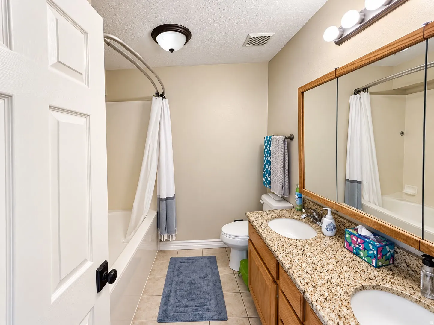 Double vanity with granite countertop and dual undermount sinks, wood-finish cabinetry, and a full-width mirror