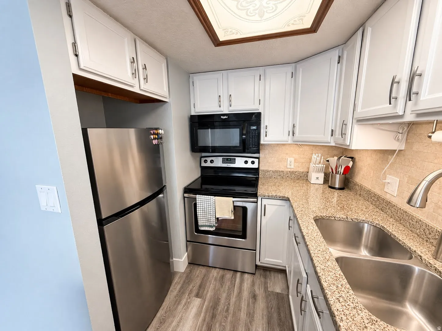 White cabinetry with brushed nickel hardware, stone countertops with a tile backsplash, stainless steel appliances, and wood-finish flooring