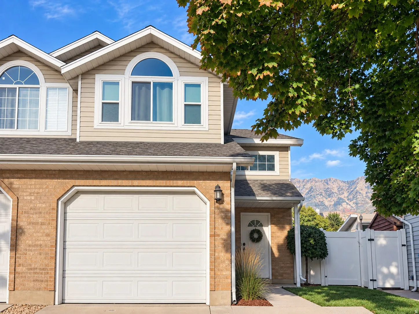 Brick and siding exterior with arched windows, an attached garage, and a white privacy fence