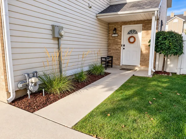 White paneled door with arched transom, brick facade around entry, concrete walkway, vibrant green lawn, and landscaped planting beds