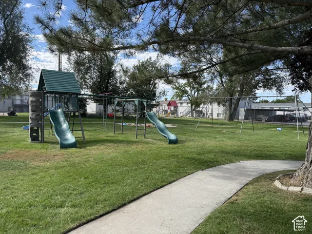 Expansive green space featuring a playground structure with slides, a swing set, and a paved pathway