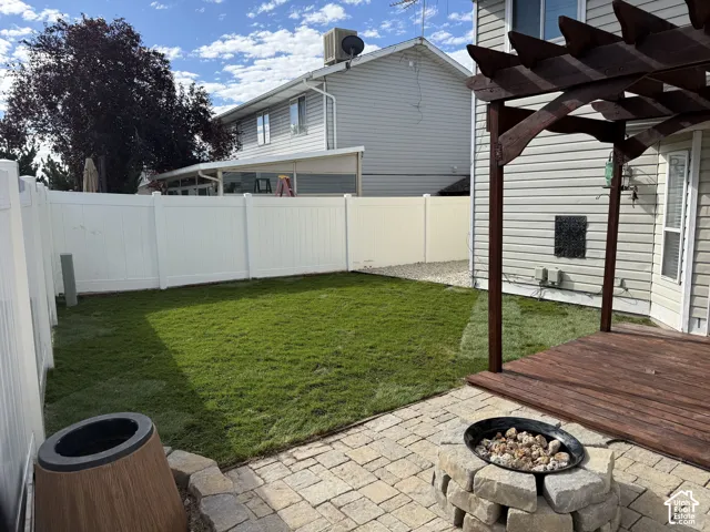 Backyard featuring a paver patio with a stone fire pit, wood deck with pergola, and manicured lawn