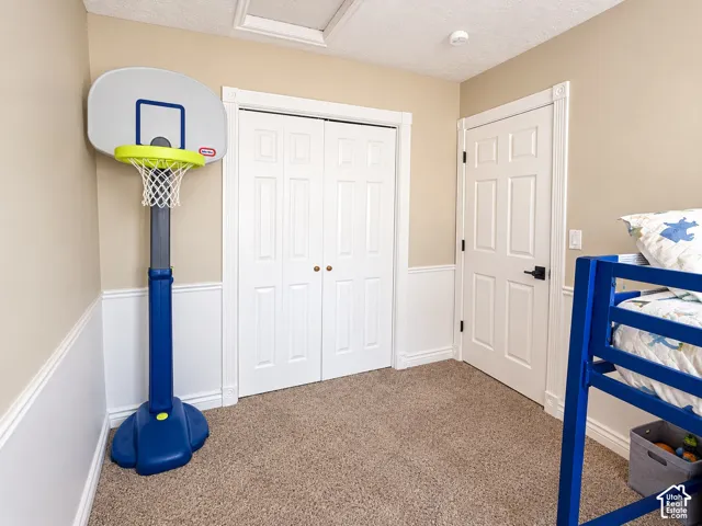 Neutral tone wall paint, white wainscoting, white bi-fold closet doors, textured carpet flooring, white paneled interior door with matte black hardware