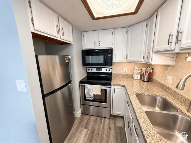 White cabinetry with brushed nickel hardware, stone countertops with a tile backsplash, stainless steel appliances, and wood-finish flooring