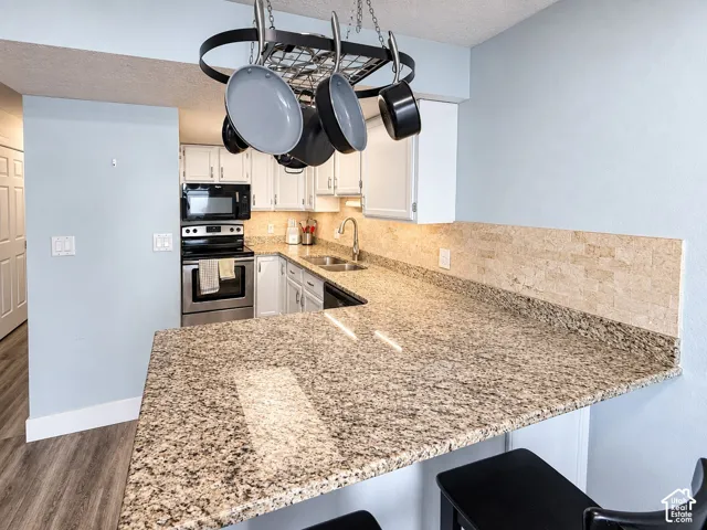Kitchen featuring granite countertops, stainless steel appliances, white cabinetry, a tile backsplash, and wood-finish flooring