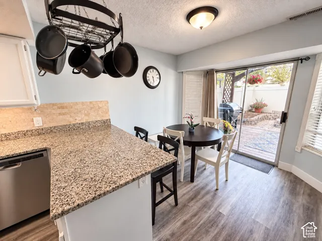Kitchen dining area featuring granite-finish countertops, stainless steel appliance, wood-finish flooring, and direct access to an outdoor patio with privacy fencing