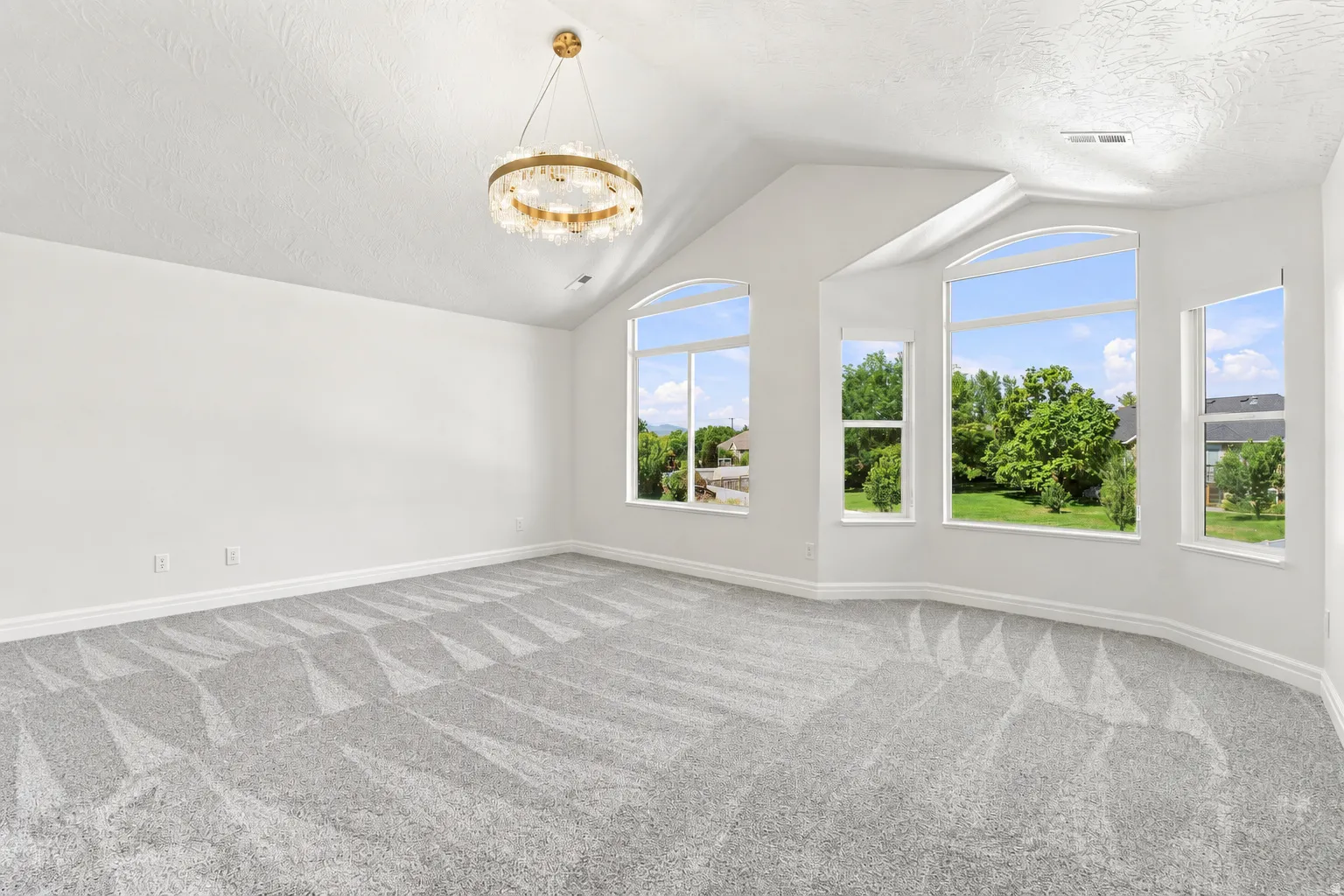 Vaulted ceiling with an ornate chandelier, multiple arched windows, patterned carpet, and white walls