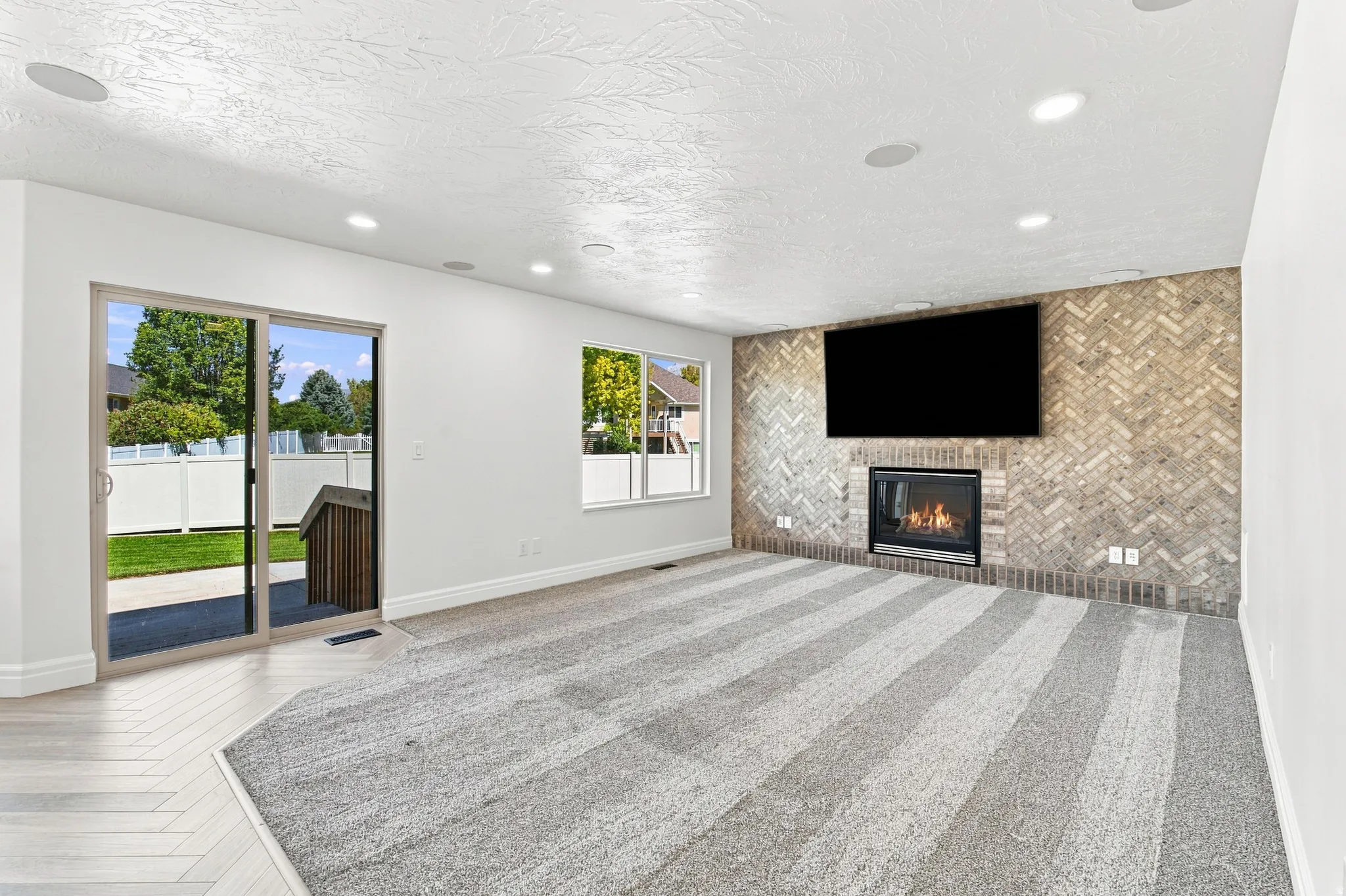 Fireplace with herringbone-patterned brick surround, recessed lighting, sliding glass door to exterior, and carpet flooring