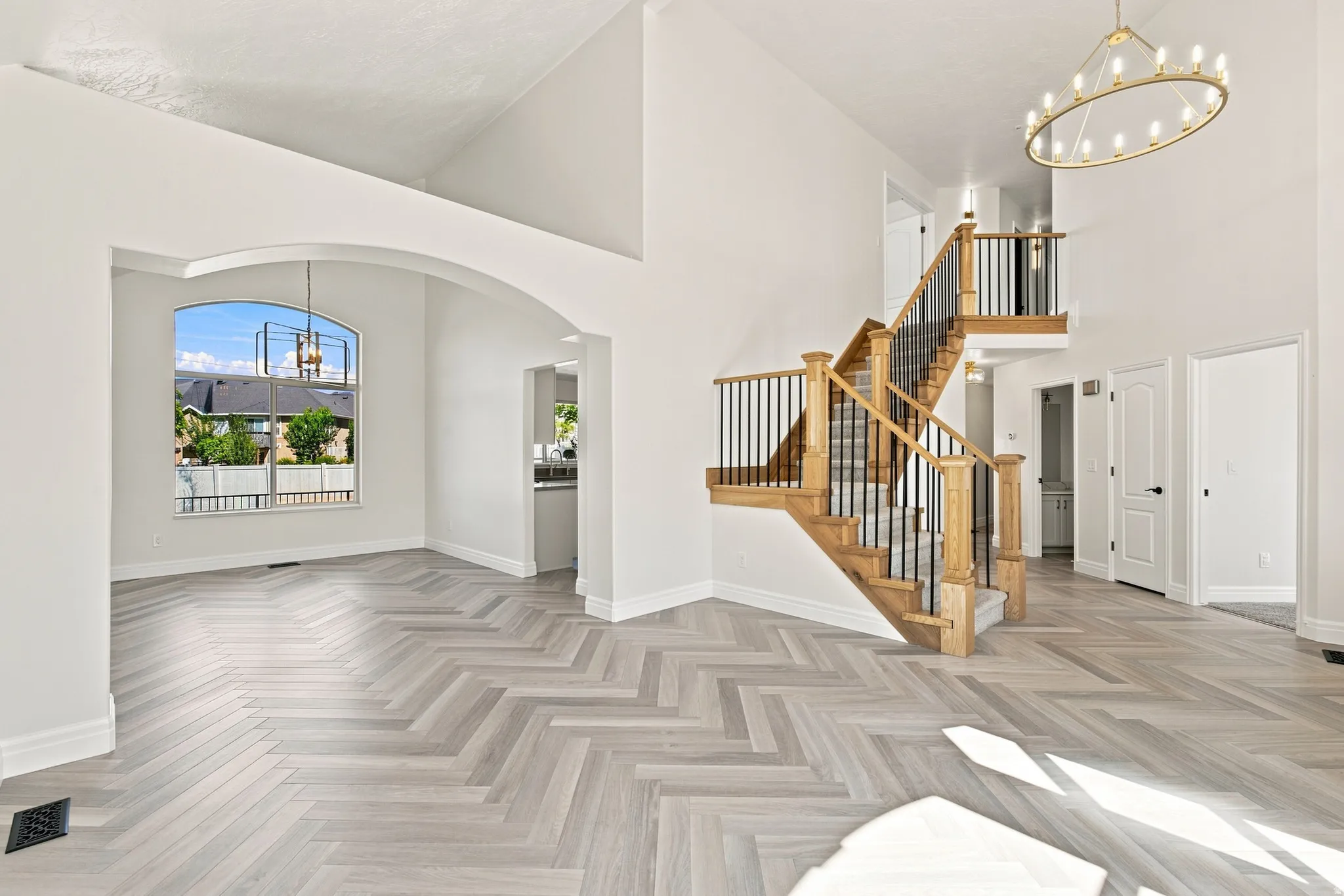 Vaulted ceilings with an arched entryway, herringbone wood-finish flooring, and an open-tread staircase with wood newel posts and iron balusters