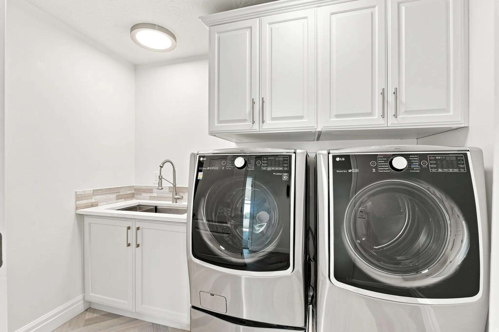 White shaker-style cabinetry, a built-in utility sink, and a tile backsplash