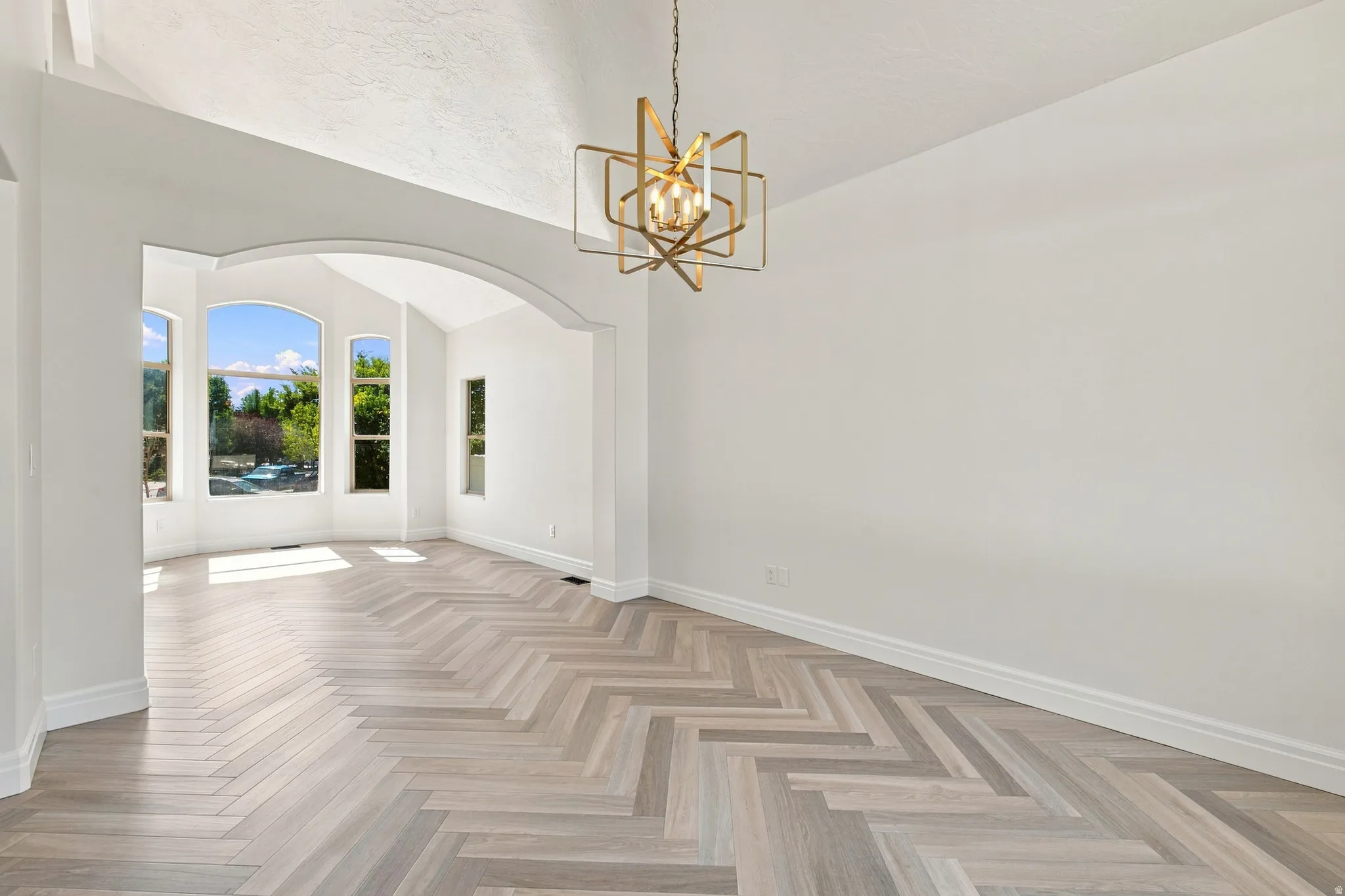 Herringbone wood-finish flooring, vaulted ceilings, arched entryways, and a contemporary chandelier