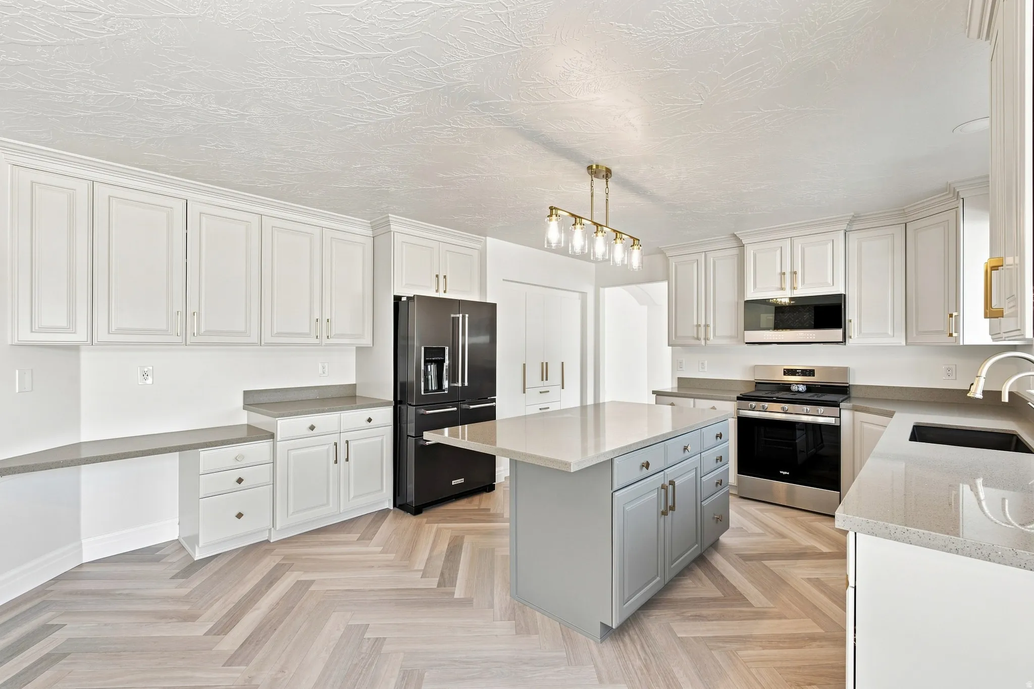 Kitchen featuring extensive white cabinetry, herringbone wood-finish flooring, a central island with countertop, stainless steel appliances, and a built-in desk area