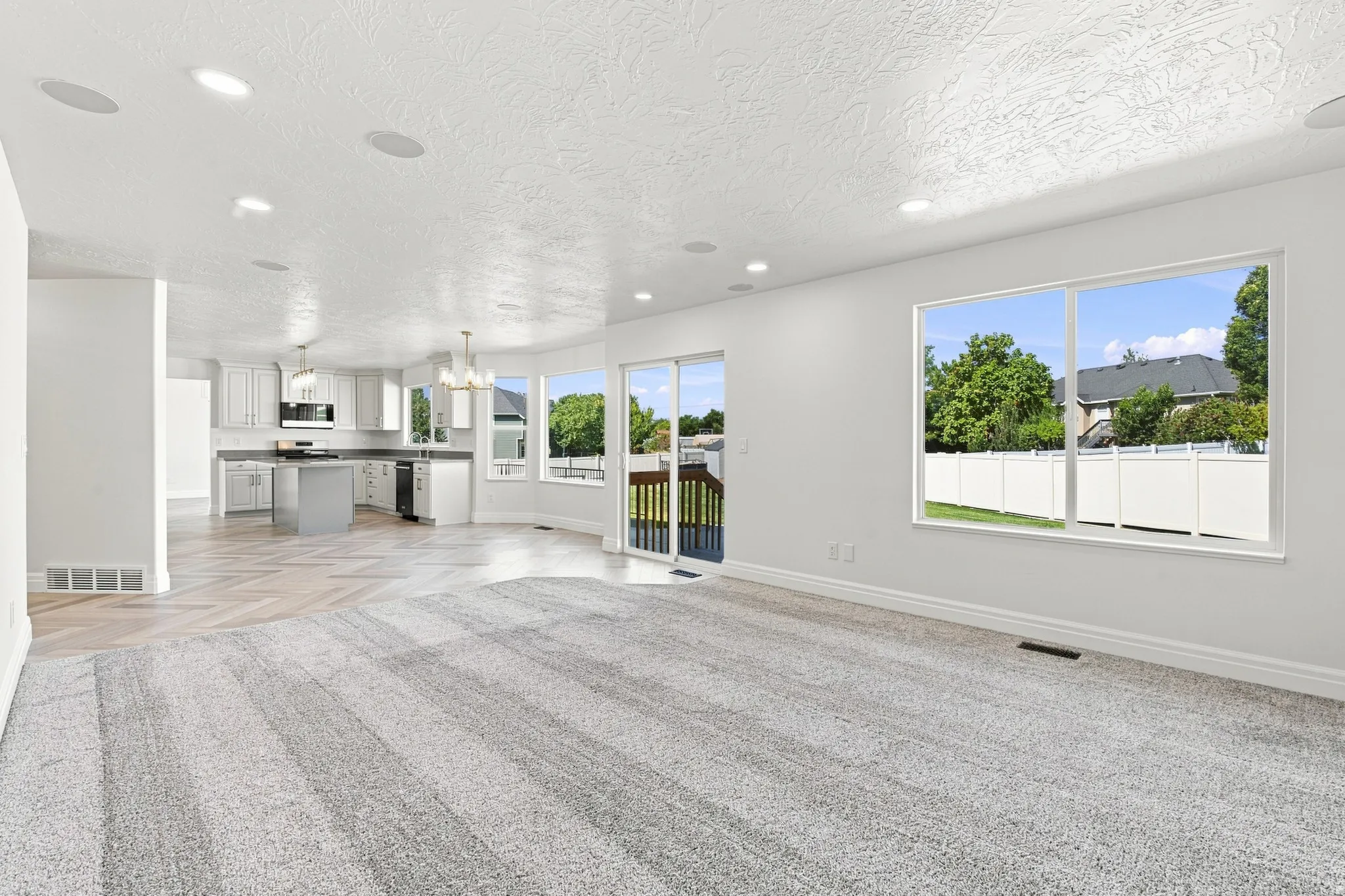 Recessed lighting, wood-finish flooring, white cabinetry, integrated kitchen appliances, and sliding glass door access to an outdoor deck