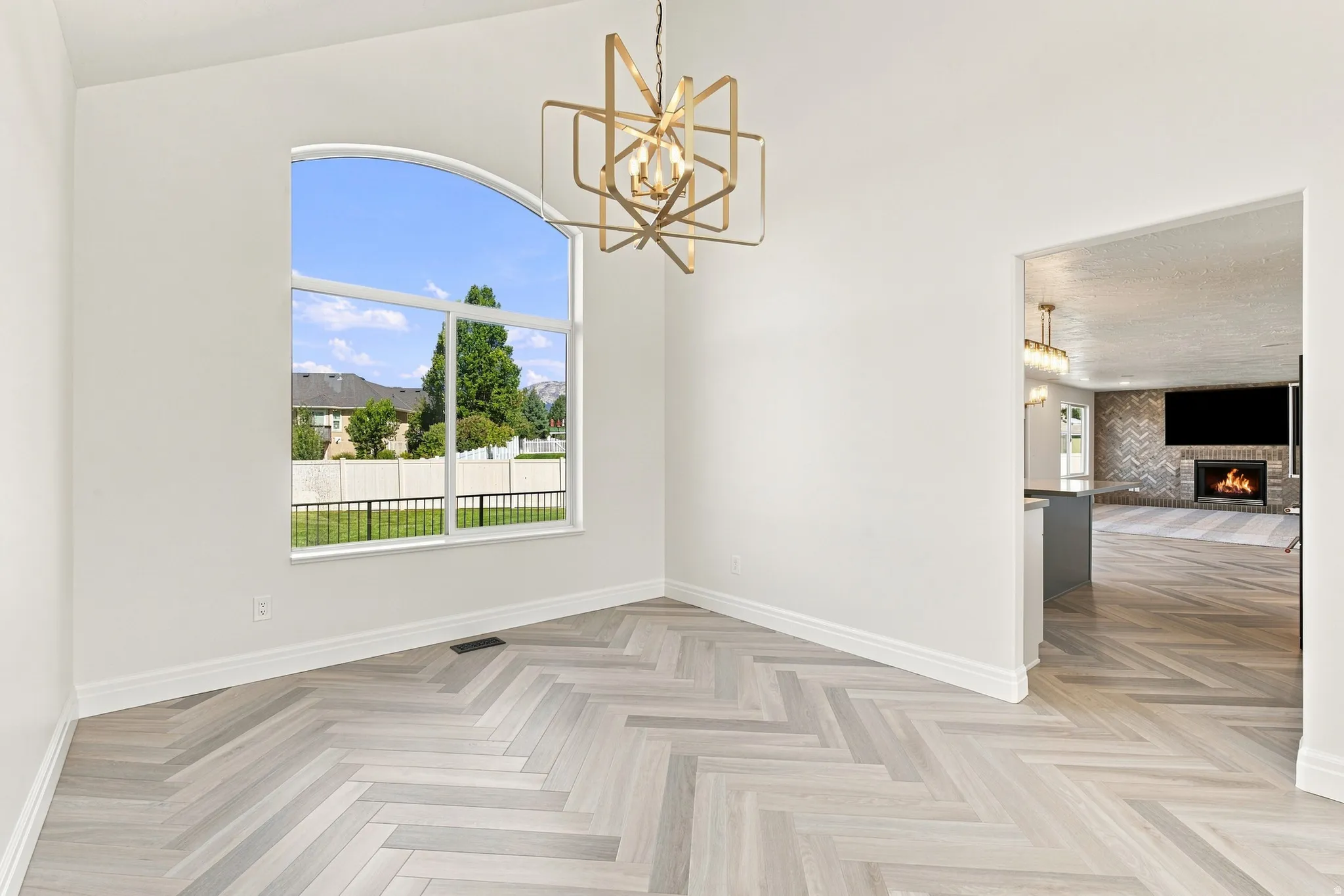 Arched window with exterior grounds, chevron-patterned wood-finish flooring, contemporary chandelier, and a recessed fireplace with decorative tile surround