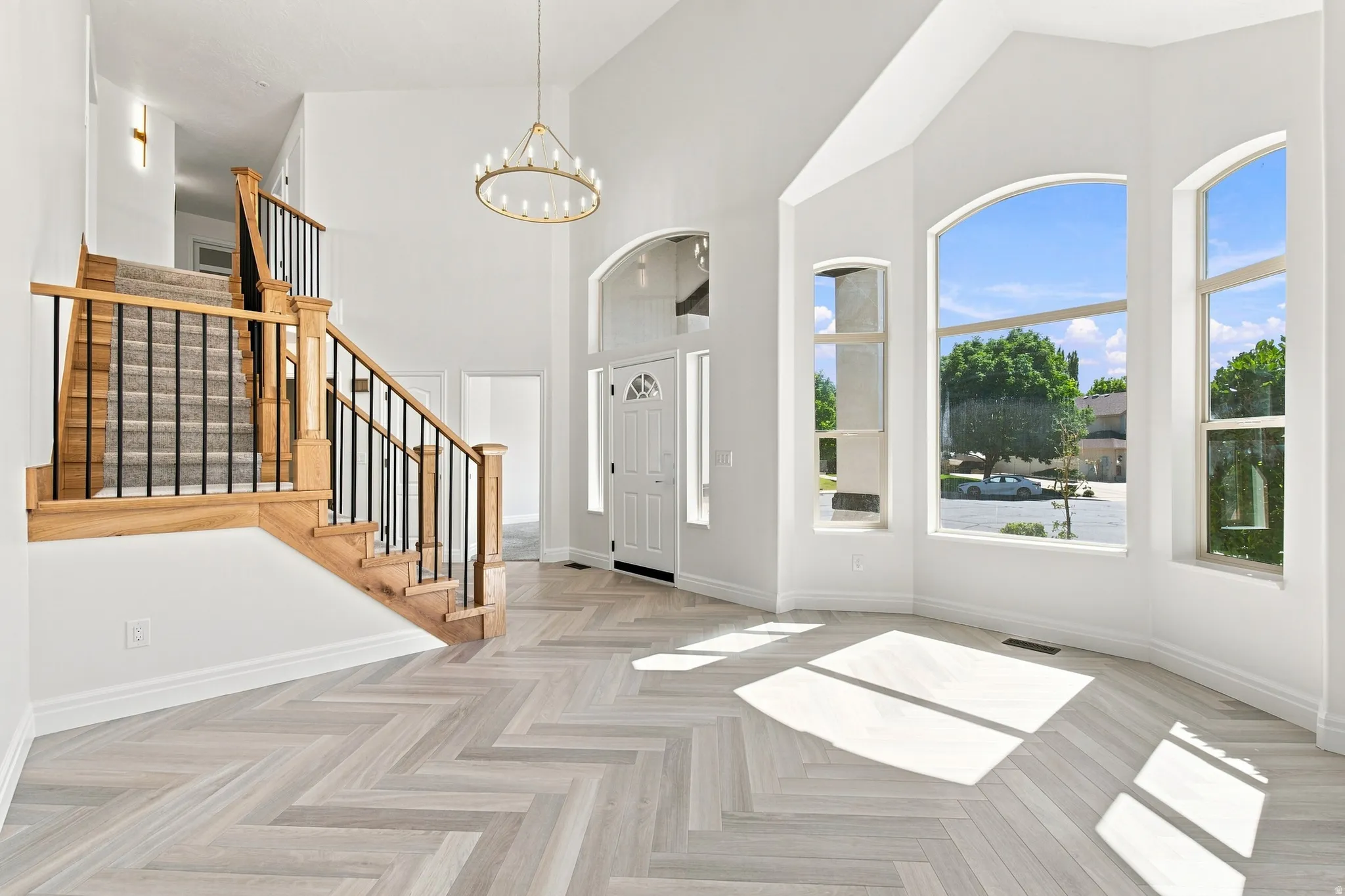 Vaulted entry with herringbone wood-finish flooring, a grand staircase featuring wood newels and wrought iron balusters, and a contemporary chandelier