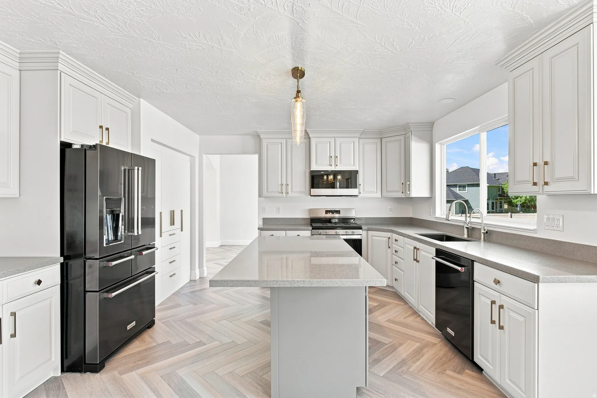 White shaker cabinetry with gold-tone hardware, a large kitchen island with a light-toned countertop, and stainless steel appliances
