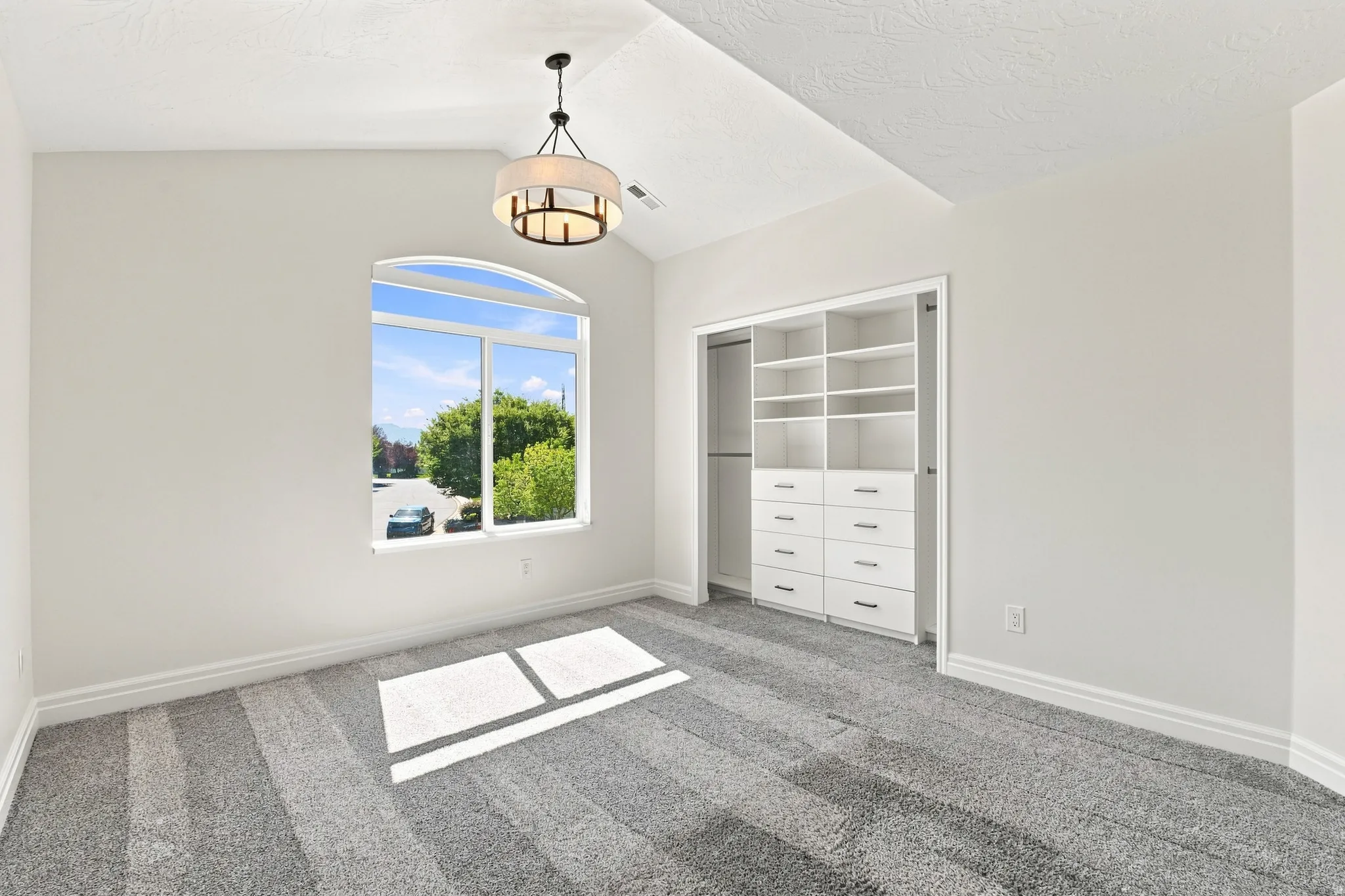 Vaulted ceiling with an attached chandelier, arch-top window, built-in closet organization system, and grey carpet flooring