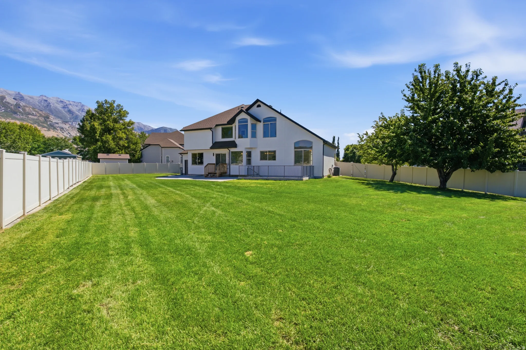 Expansive backyard featuring a manicured lawn, a full vinyl privacy fence, and mature trees