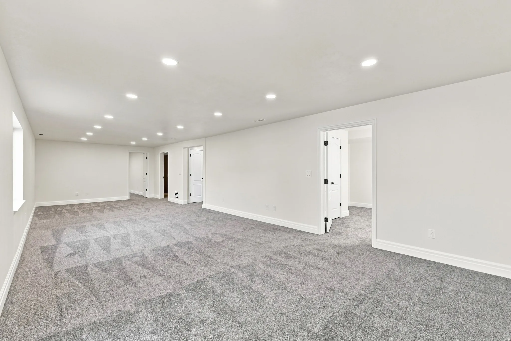 Expansive room with recessed lighting, light gray patterned carpet, white walls, and multiple doorways