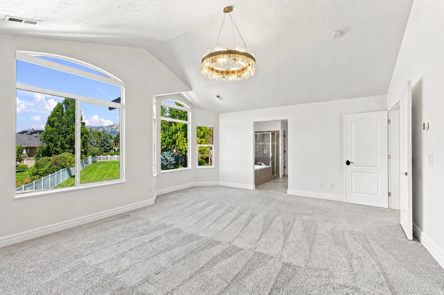 Arched windows, vaulted ceiling, crystal chandelier, neutral wall paint, and soft gray carpeting