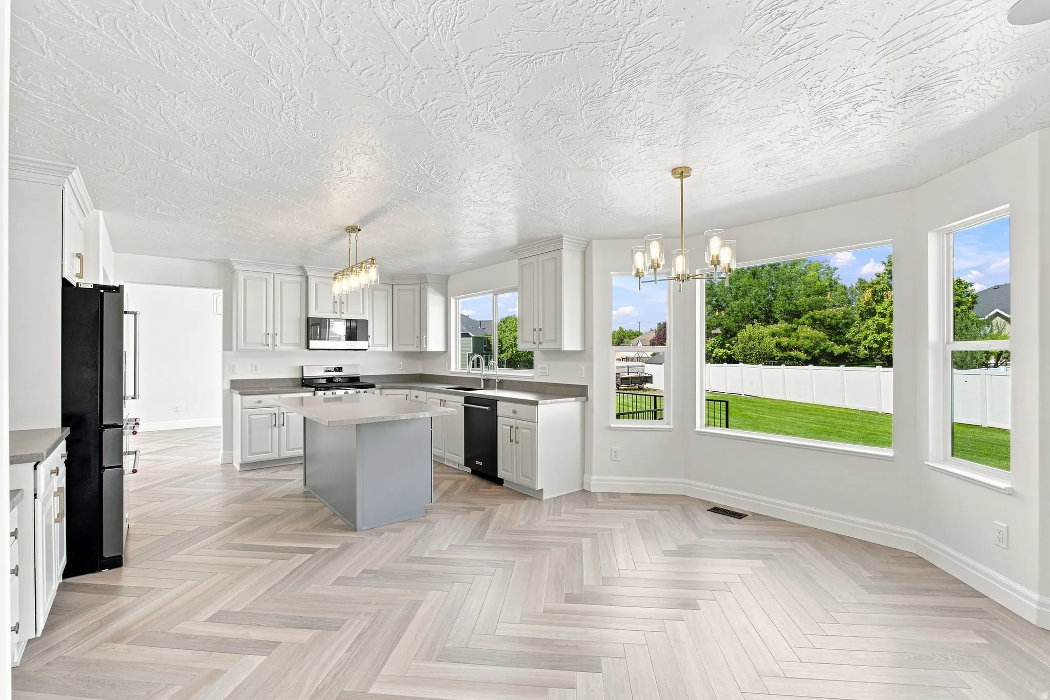 Contemporary kitchen featuring white cabinetry, a center island with a stone countertop, a full suite of black appliances, and light-toned wood-finish flooring in a herringbone pattern