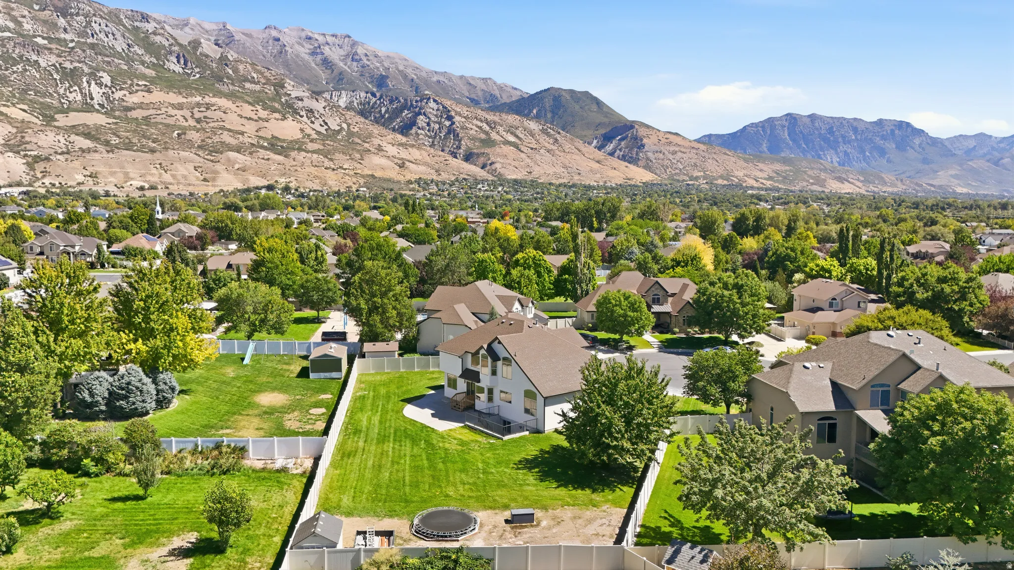 Expansive property featuring a multi-story residence, a large green lawn, and a white perimeter fence