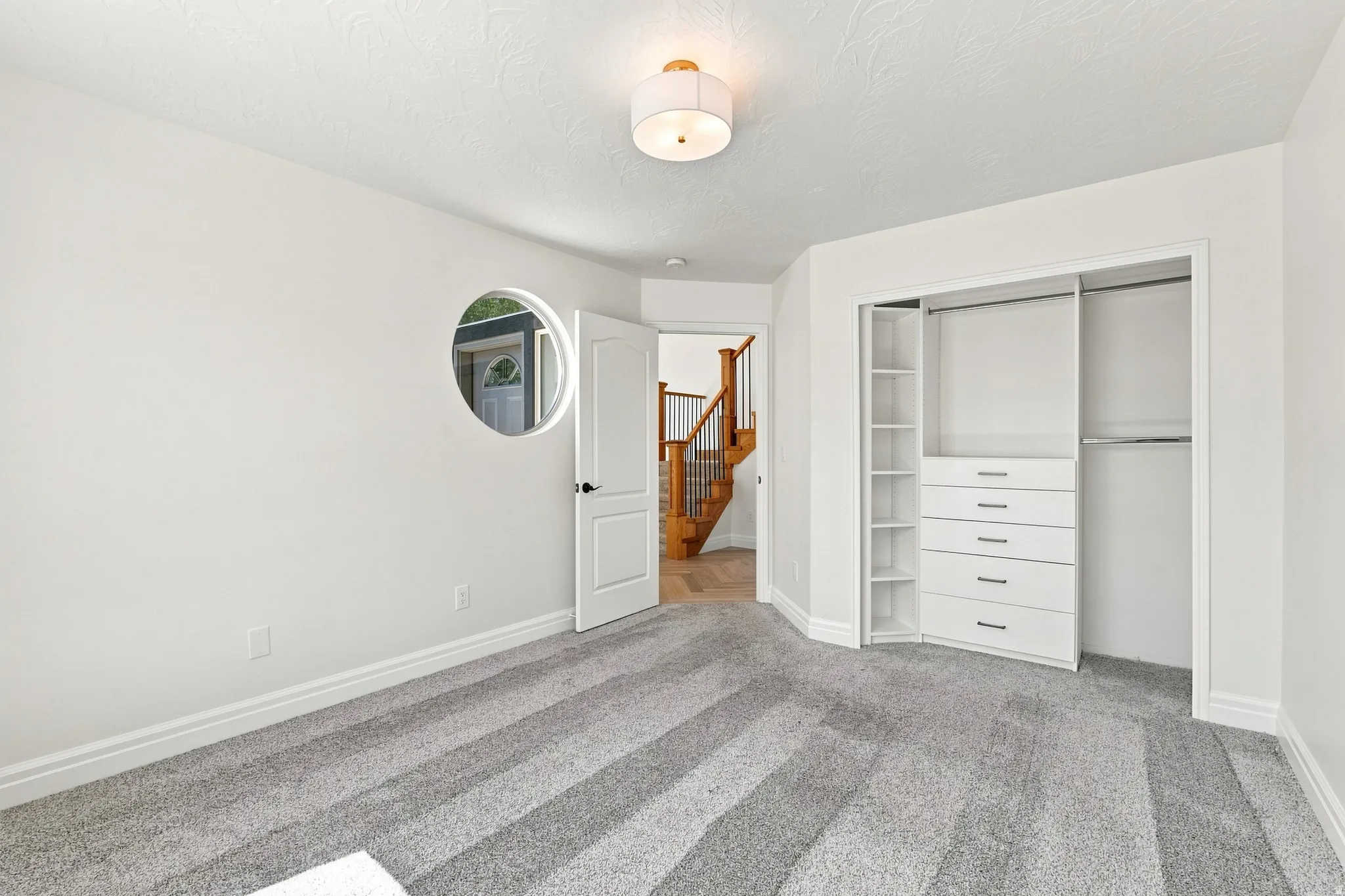 Built-in closet organization system, modern ceiling light fixture, accent round wall cut-out, white paneled interior door, and grey patterned carpet flooring